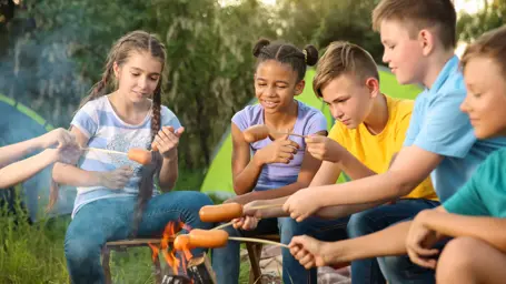 Group of children cooking sausages around a campfire