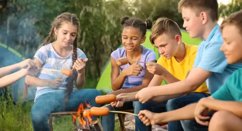 Group of children cooking sausages around a campfire