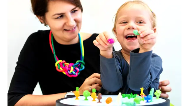 Child playing with toys on a peg board with a woman helping her