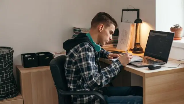Teenager writing notes while on laptop